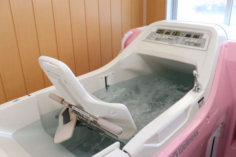 介護施設の温浴療法機器。ピンク色の入浴補助装置で、温度制御パネルが装備されている。